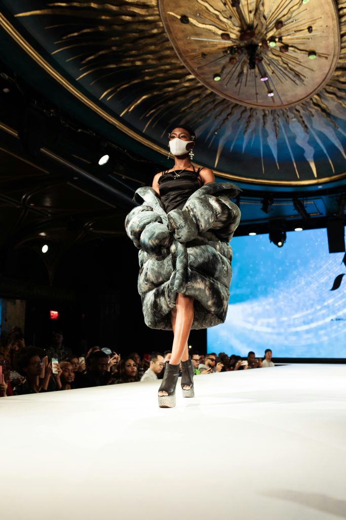 Stunning fashion model walks the runway in an elegant fur coat and mask at a fashion show.